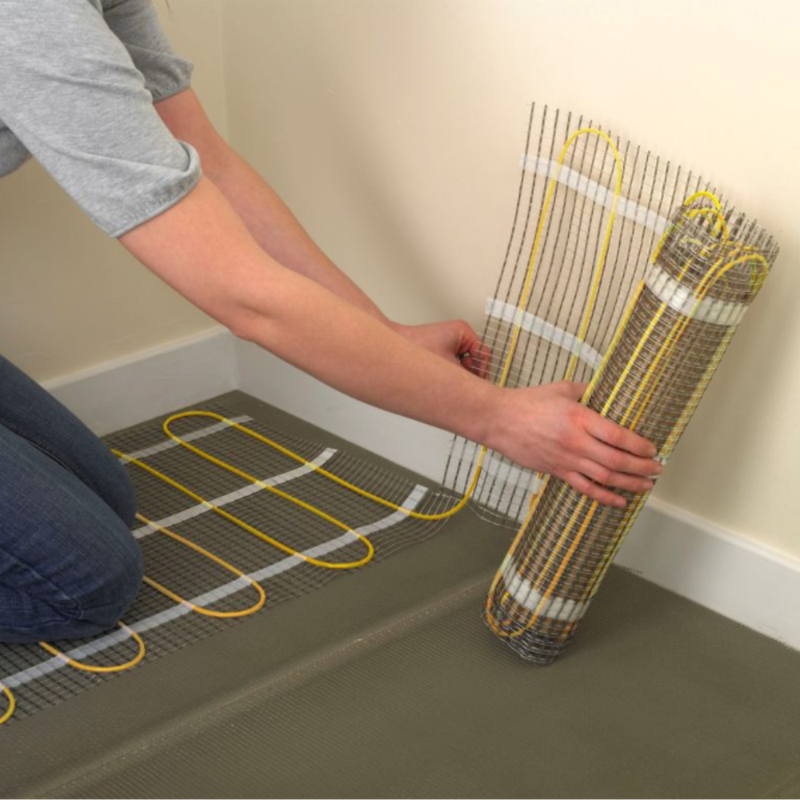 Person installing a roll of electric floor heating cable on a concrete floor.