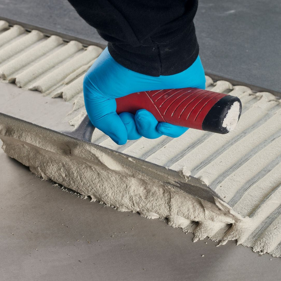 Person applying tile adhesive to a surface with a trowel