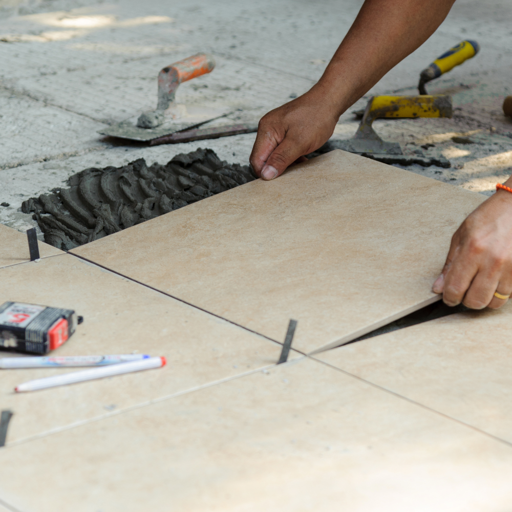 Person installing tiles with tools on a concrete floor