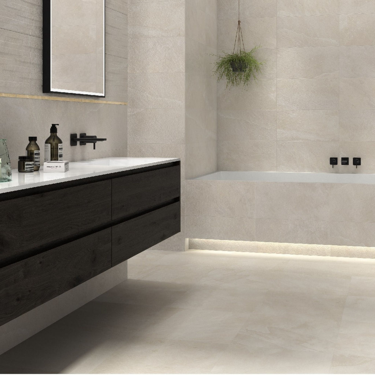 A modern bathroom interior with Lannion Blanco large white stone effect tiles on walls and floors, a floating dark wood vanity with a white countertop, a black faucet, a built-in bathtub, and a hanging green plant.