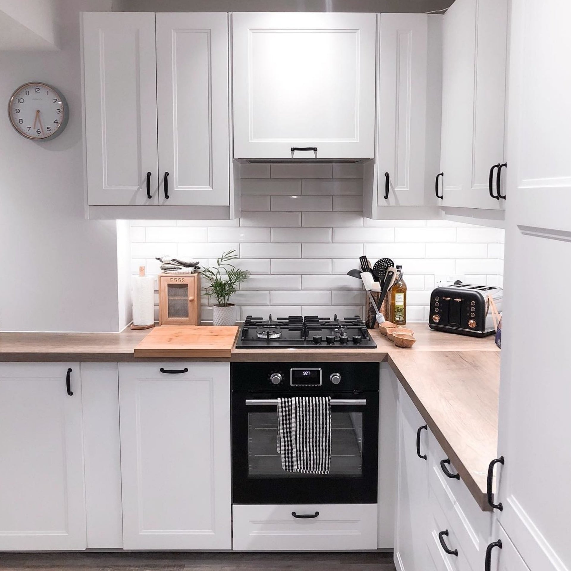 Modern minimalist kitchen with white cabinets, white brick tiles backsplash, black appliances, and wooden countertops.