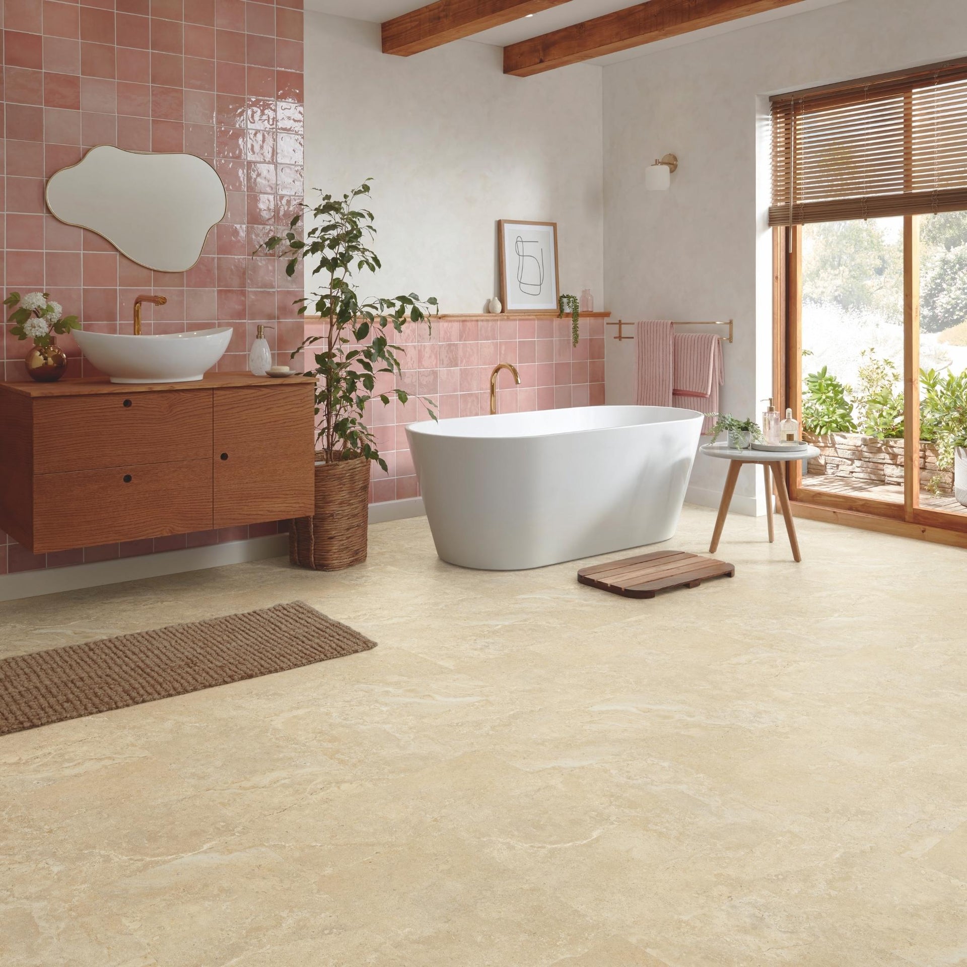 Modern bathroom with freestanding bathtub, wooden vanity, pink tiled wall, and travertine beige stone effect LVT floor tiles.