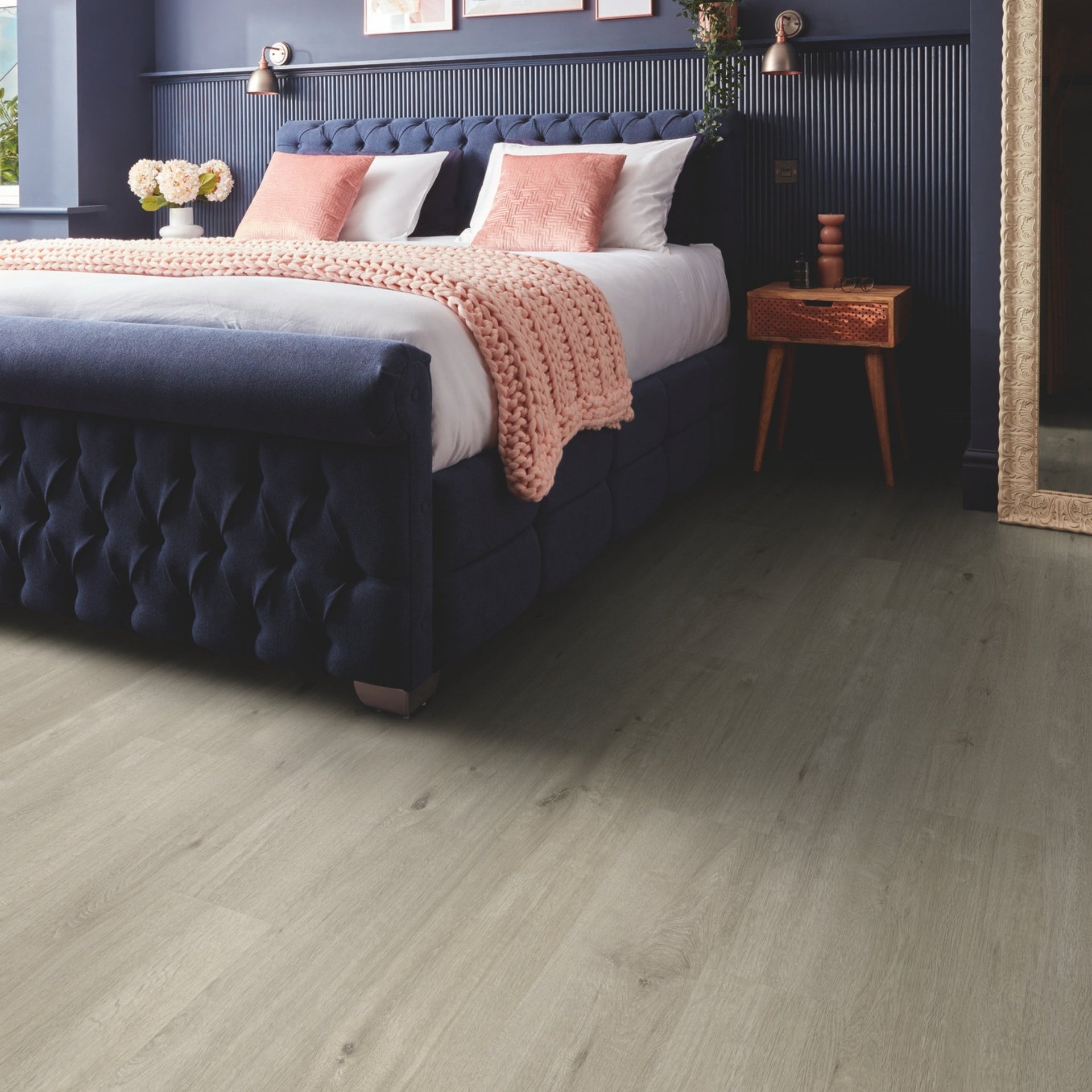 Navy bed with pink blanket and pillows in a bedroom setting on a greige wood effect floor luxury vinyl tiles

layout-bedroom