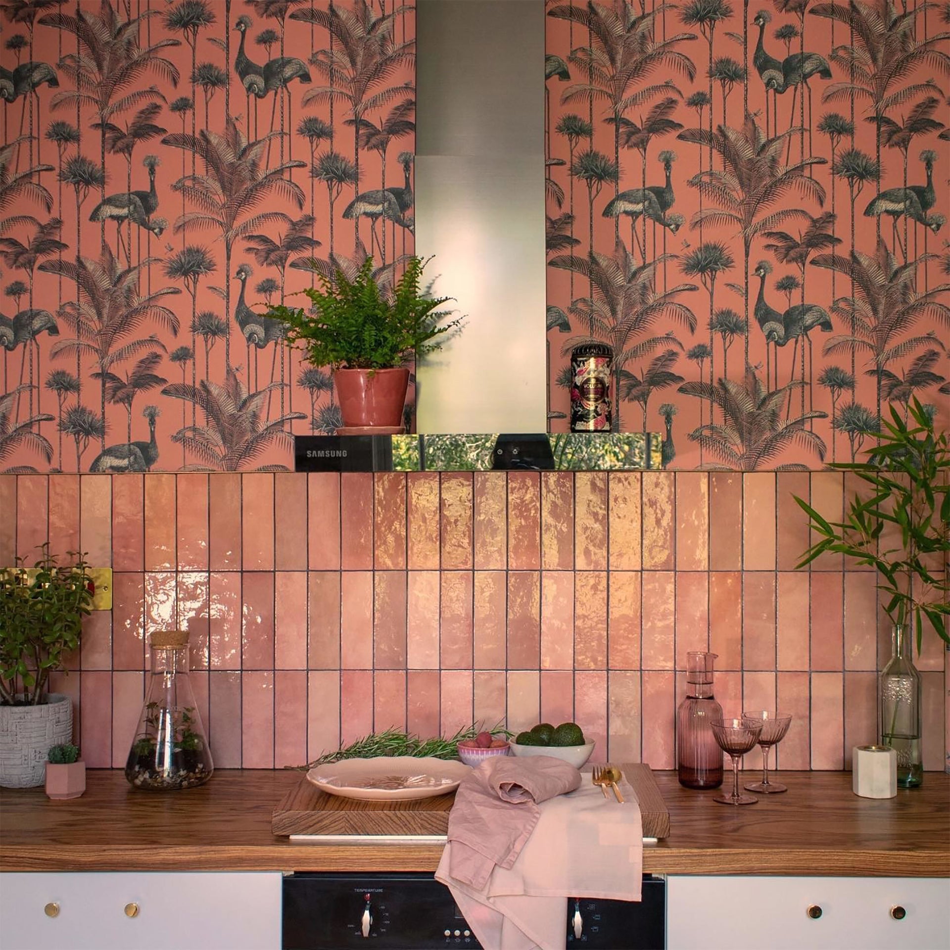Handmade-effect pink glossy tile flooring in an interior kitchen setting, with decorative plants and items around.
