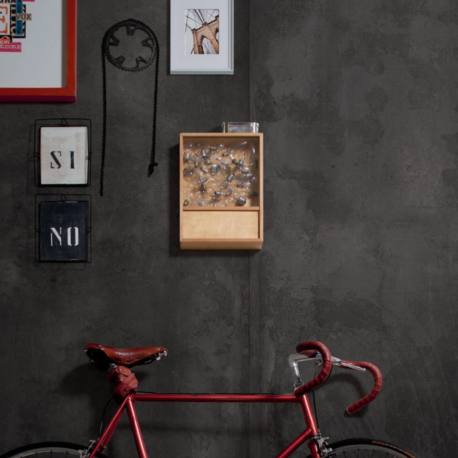 Red bicycle against a black dark concrete effect wall and floor tiles, with decorative wall frames.