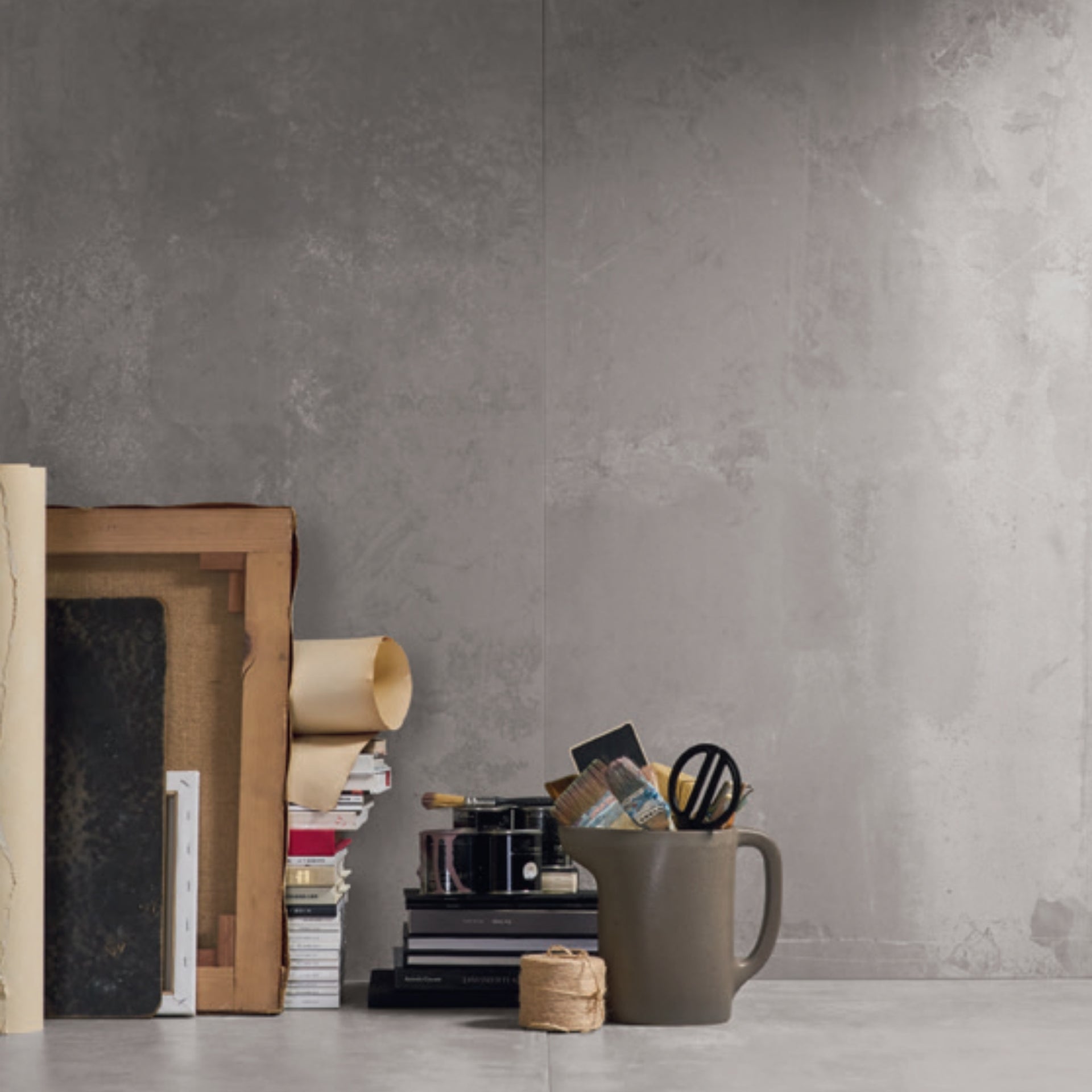 Grey concrete effect textured wall and floors with a shelf holding books, a pitcher, and stationery against a neutral background.
