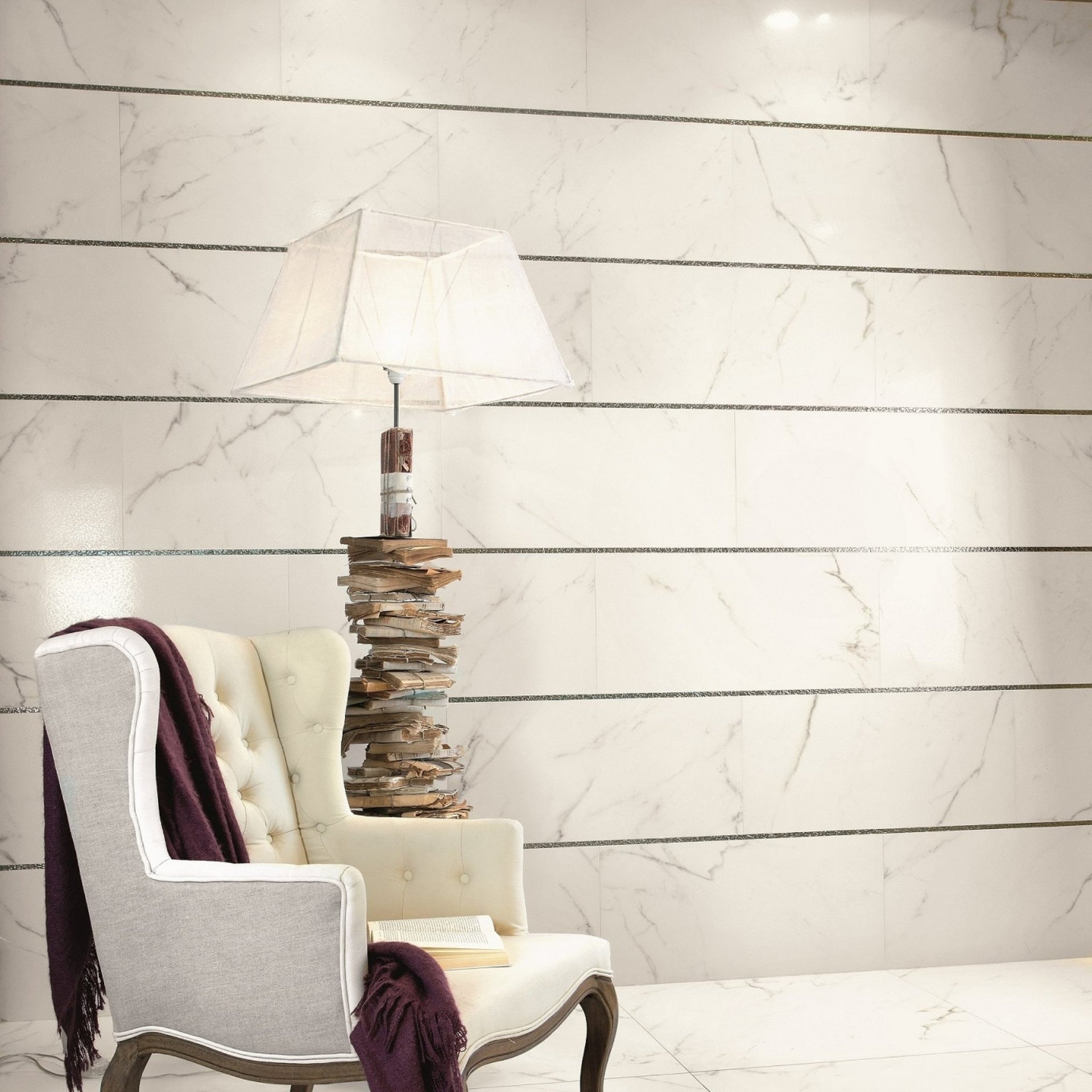 Decorative lamp with a bookshelf base on a Carrara marble-patterned wall tiles with listello strips.