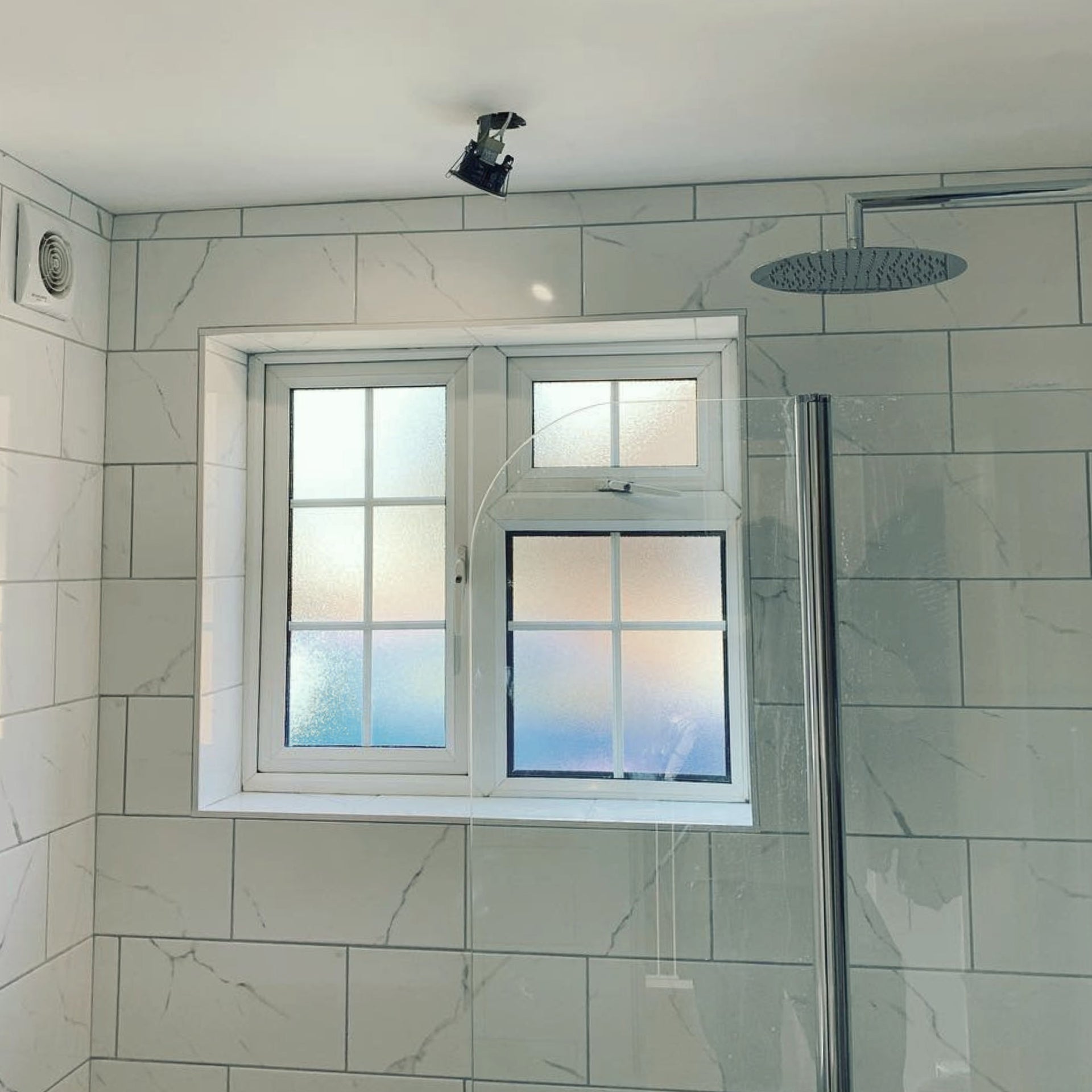 Shower enclosure with a window in a marble white tiled bathroom