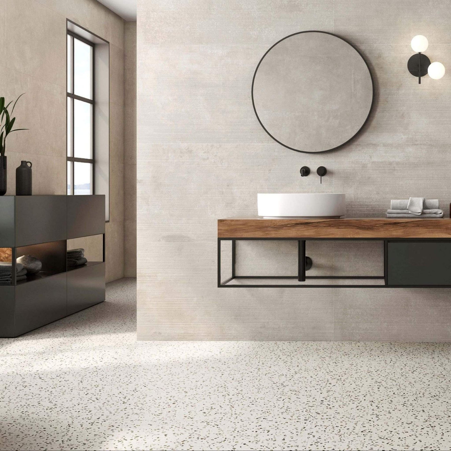 Modern bathroom with wooden vanity, round mirror, and neutral decor on terrazzo speckled grey tiles.