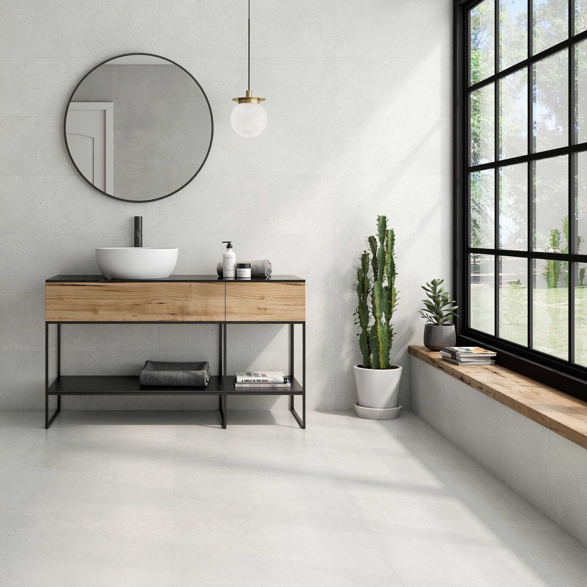 Modern bathroom with large white stone effect wall and floor tiles, on a wooden vanity, round mirror, and large window.