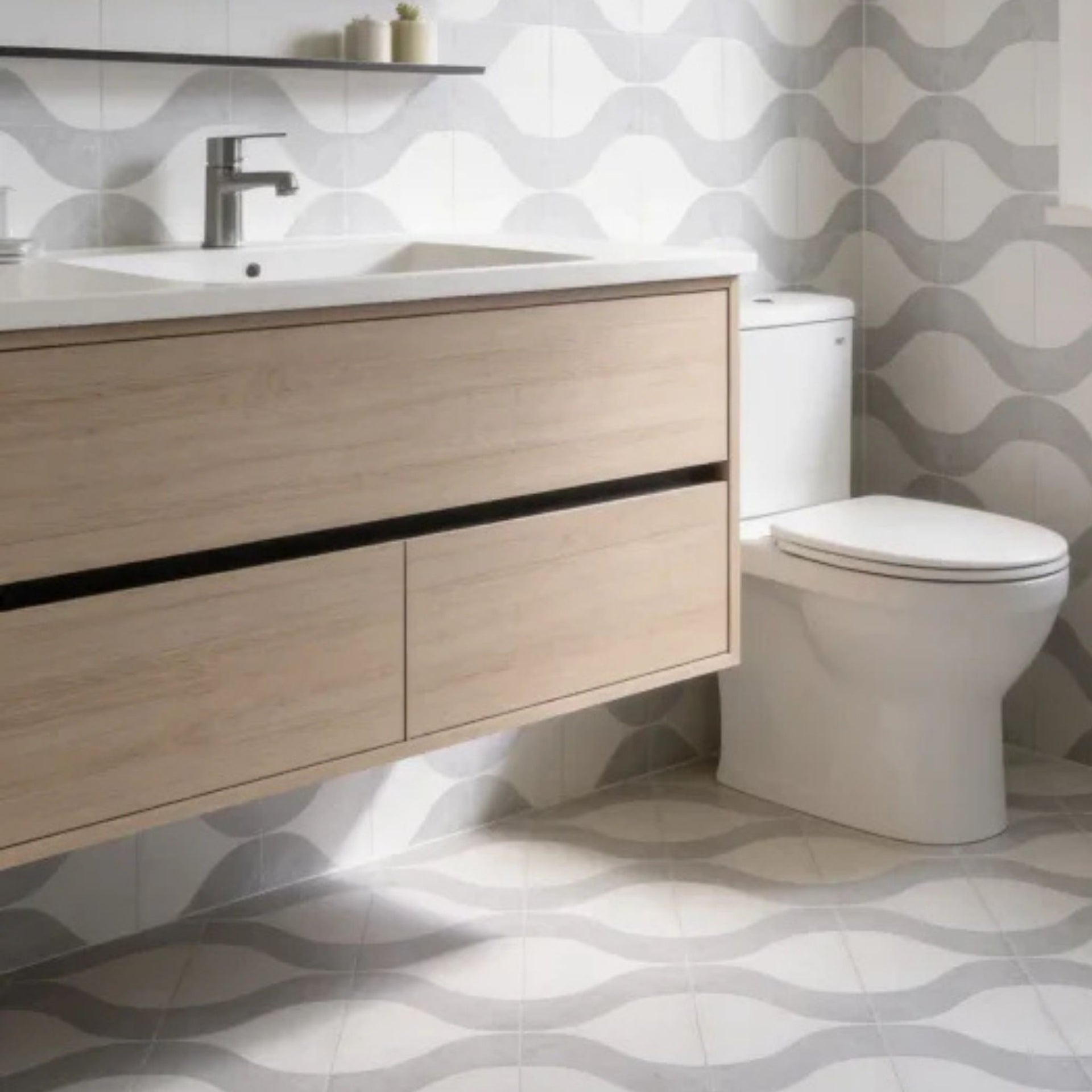 A modern bathroom scene featuring a floating light wood vanity with a white sink and chrome faucet, positioned next to a white toilet. The background and floor are decorated with gray and white Liliana wavy patterned tiles.

layout-bathroom