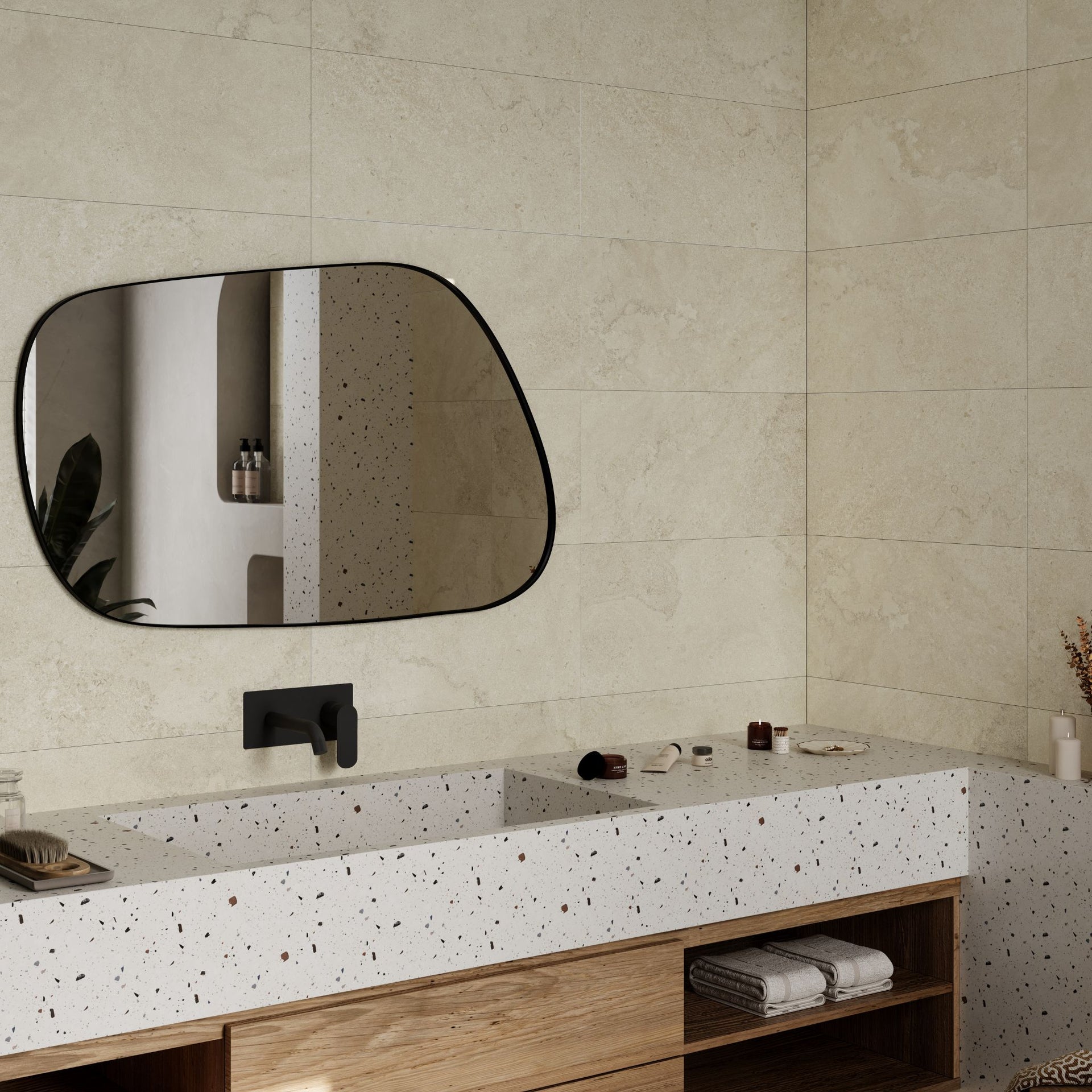 An organic-shaped wall mirror with a black frame hangs on an Oxton bone beige tiled bathroom wall above a white speckled countertop with a wooden vanity.