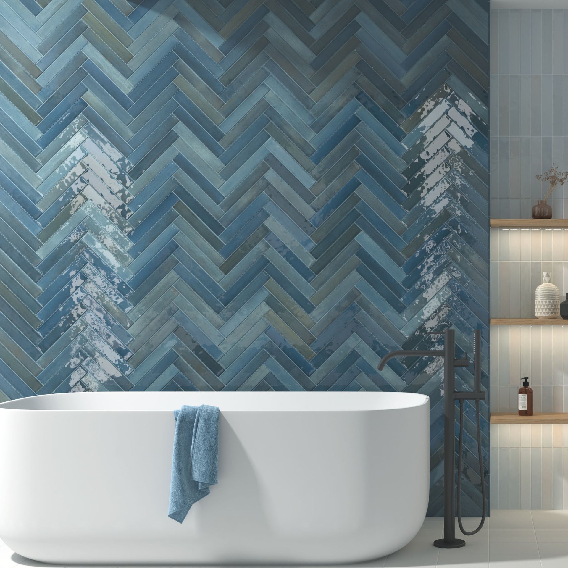 Modern bathroom with a white freestanding bathtub against a blue Tortosa gloss tonal metro tiles in herringbone chevron pattern on walls.