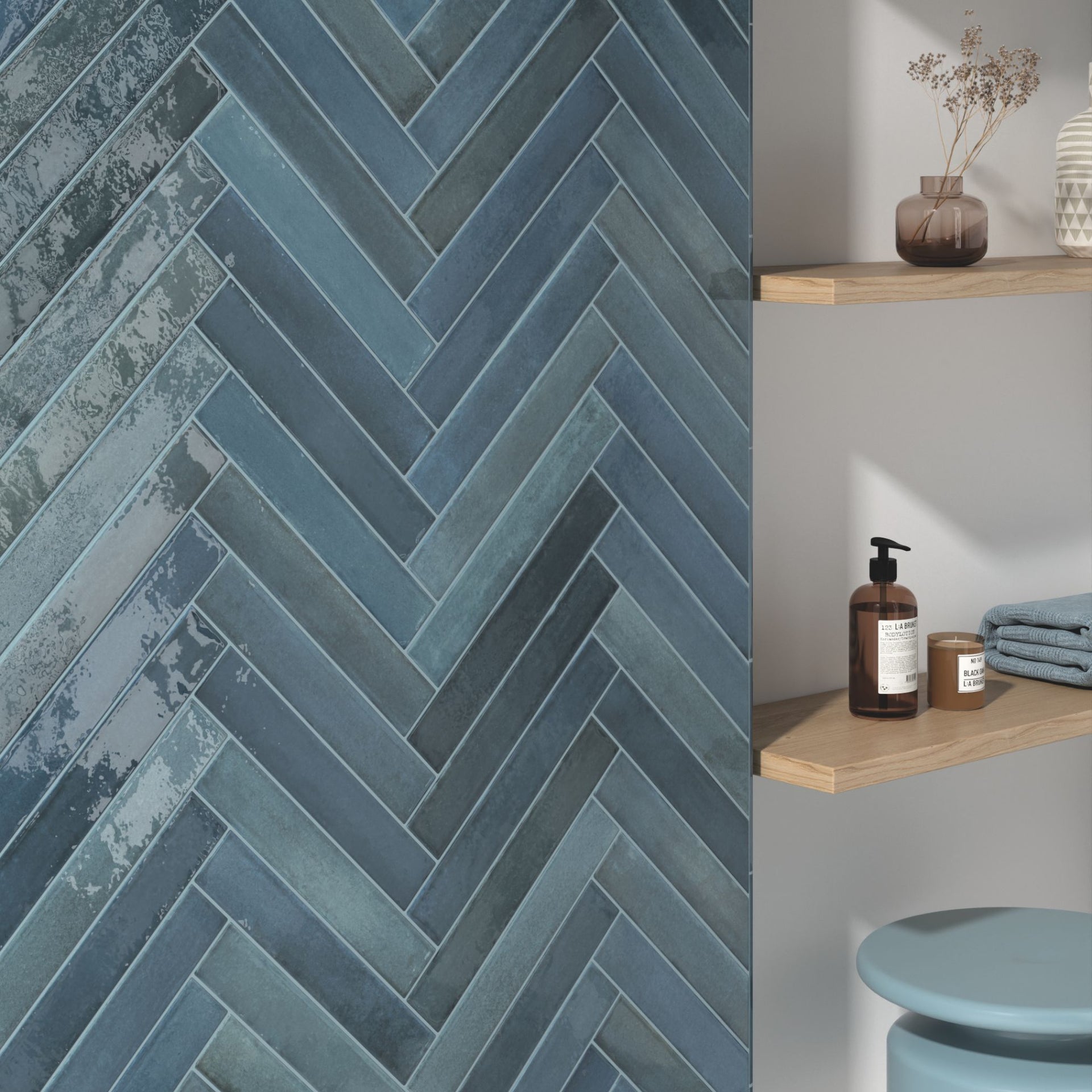 Glossy blue herringbone patterned tonal metro tile on a wall with a shelf and decorative items in the background.
