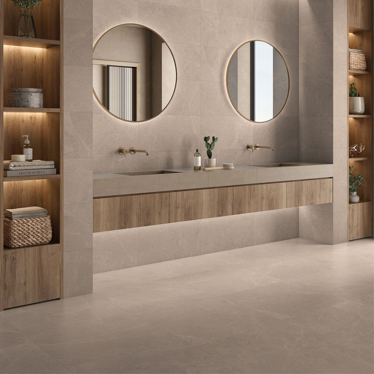 A modern bathroom vanity setup with two round backlit mirrors, a floating wood-and-sand double sink countertop, and built-in wooden shelving on both sides, on Zamora beige wall and floor tiles.